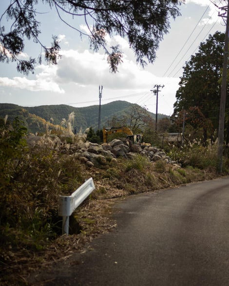 Road, brush off to the left, guardrail, digger back behind a mound of rocks.